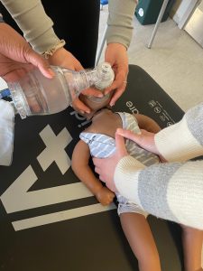 Basic Life Support training showing infant ventilation using bag-valve mask on a baby manikin