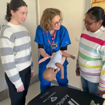 Baby first aid training session showing instructor demonstrating infant choking response to parents using a training manikin