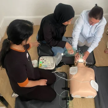 Basic Life Support training session showing CPR compressions and AED use on a manikin by participants