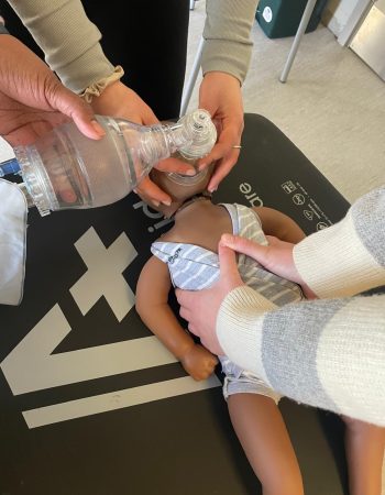 Basic Life Support training showing infant ventilation using bag-valve mask on a baby manikin