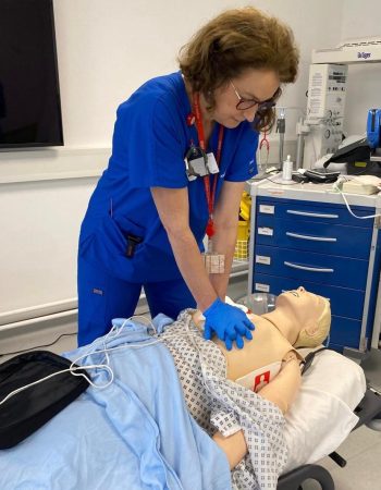 ILS training session showing healthcare professional performing CPR and AED pad placement on a manikin in a clinical setting